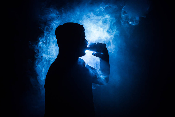 Vaping man holding a mod. A cloud of vapor. Black background. Vaping an electronic cigarette with a lot of smoke. Vape concept - Foto, Imagem