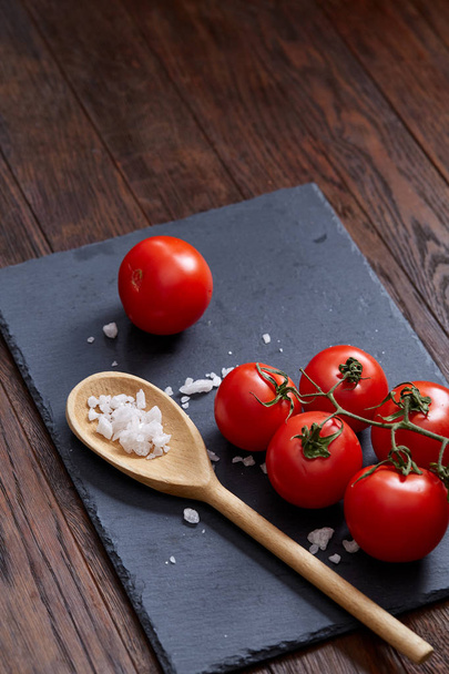 Vegetarian still life with fresh grape tomatoes, pepper and salt in wooden spoon on wooden background, selective focus - Foto, immagini