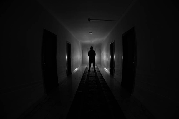 Silhouette effrayante dans le bâtiment sombre abandonné. Couloir sombre avec portes d'armoire et lumières avec silhouette d'horreur effrayant personne debout avec différentes poses
. - Photo, image