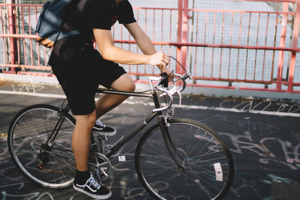 Sportieve man in moderne koptelefoon luisteren elektronische muziek bevrijden op fiets. Aziatische man gekleed in zomer kleding met rugzak opleiding op twee wielen buitenshuis in stedelijke omgeving - Foto, afbeelding