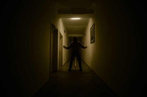 Темний коридор з кабінетними дверима і вогнями з силуетом жахливого чоловіка, що стоїть з різними пози
. - Фото, зображення