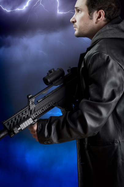 Man with long leather jacket and assault rifle over storm backgr - Foto, imagen