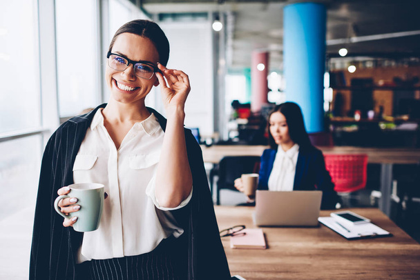 Half length portrait of prosperous female company owner in formal wear enjoying coffee in office,cheerful young business woman in elegant outfit and spectacles satisfied with successful career - Foto, Bild