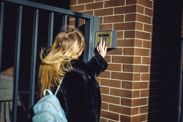 young blond woman in a fur coat, dials the code on the doorphone panel, presses  buttons with her fingers to get inside house - Photo, image