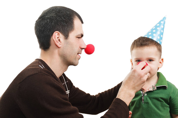 Vader en zoon in een feestelijke kegel en een clown's neus - Foto, afbeelding