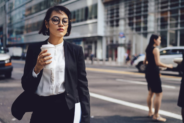 selbstbewusste Geschäftsfrau in formeller Kleidung eilt zu Fuß zum Büro in der Nähe der Werbefläche für geschäftliche Information.Managerin in stilvoller Brille spazieren in New York City, während Kaffee nach draußen gehen - Foto, Bild
