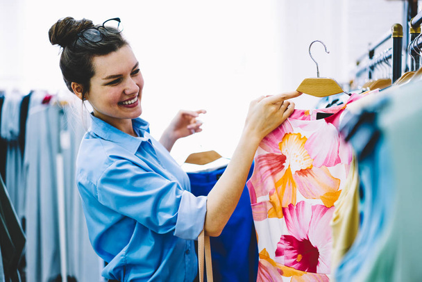 Happy female designer choosing dresses for own new collection standing in showroom with colorful clothing in hands.Fashion stylist working with production of trendy textile for development busines - Fotoğraf, Görsel