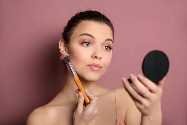Mujer joven que aplica maquillaje sobre el fondo de color. Productos cosméticos profesionales
 - Foto, imagen
