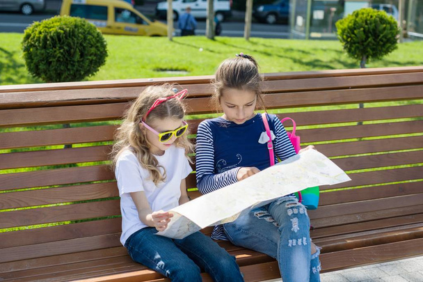 Outdoors portrait children tourists. With map of city on the bench - 写真・画像