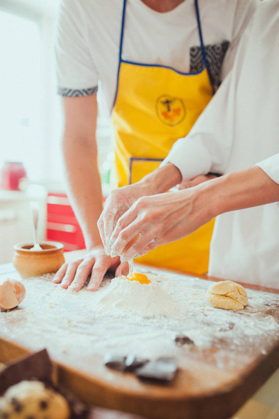 Handen van mannelijke en vrouwelijke chef-kok close-up, kneed het deeg, het deeg op een keuken koken. - Foto, afbeelding