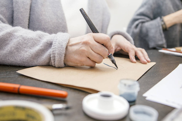 Женщина делает каллиграфические надписи, рисует на бумаге ручкой b
 - Фото, изображение