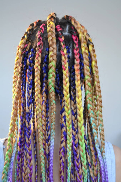 Een meisje met een modieuze set van veelkleurige vlechten Kanekalon. Gekleurde kunstmatige strengen van het haar. Materiaal voor vlechtwerk vlechten. - Foto, afbeelding