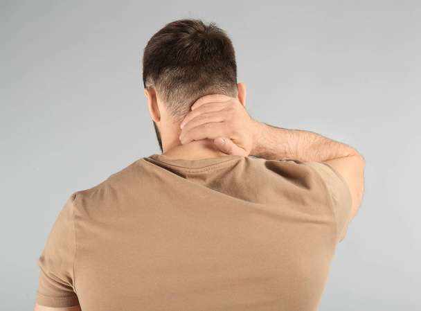 Молодой человек страдает от боли в шее на светлом фоне
 - Фото, изображение