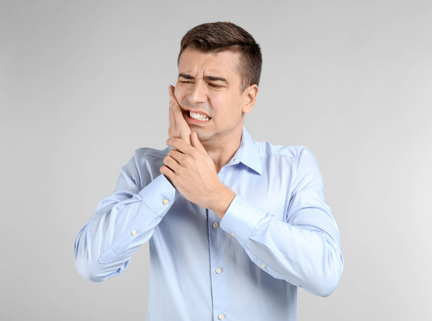 Young man suffering from toothache on light background - Photo, image