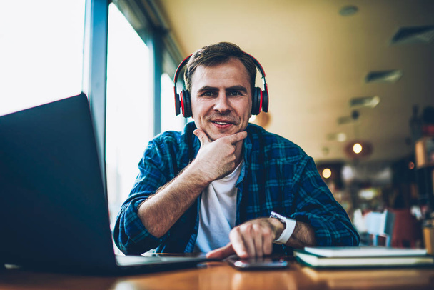 Half length portrait of handsome smiling freelancer taking working break and listening to favorite playlist via headphones.Young positive man looking at camera while enjoying free time with music - Foto, imagen