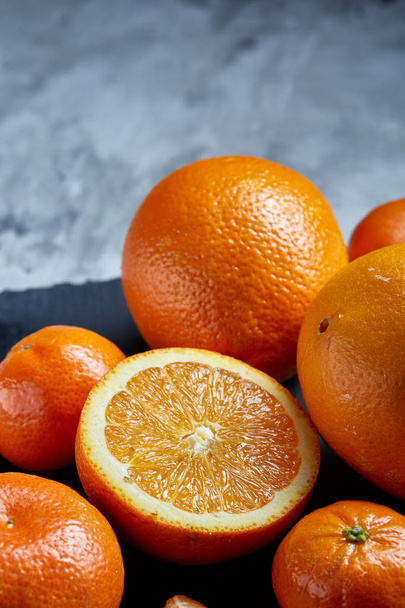 Pile of whole and half cut fresh tangerine and orange on cutting board, close-up - 写真・画像