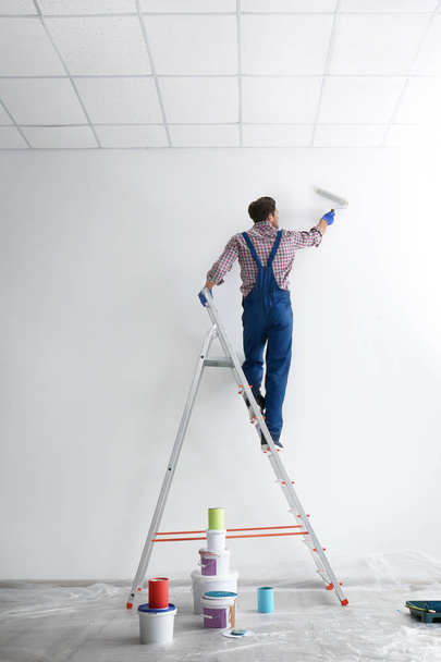 Male decorator painting wall with roller in empty room - Fotó, kép