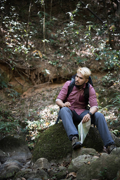 Nuori väsynyt retkeilijä reppu istuu kivellä metsässä lepäämässä aktiivisen kävelyn jälkeen. Matkustuskäsite
 - Valokuva, kuva