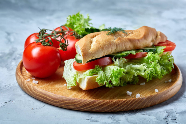 Fresh sandwich with lettuce, tomatoes and cheese served on wooden plate over white textured background, selective focus - 写真・画像