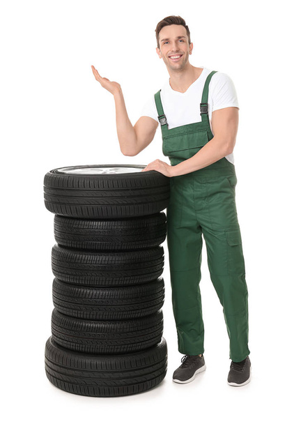 Young mechanic in uniform with car tires on white background - Valokuva, kuva