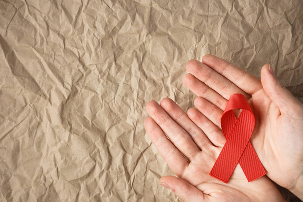 aids red ribbon on a palm and on a craft background, hiv ribbon on kraft paper - Photo, Image