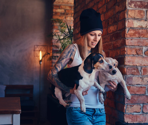 Ένα κομψό τατουάζ ξανθιά γυναίκα στο t-shirt και τζιν με τα σκυλιά - Φωτογραφία, εικόνα