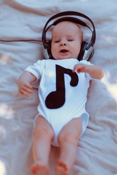 Baby in big headphones lying on bed - Foto, Imagen
