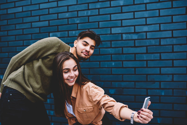 Couple in love having fun together making photo on smartphone camera near wall promotional background, best friends posing for selfie for blogging in social networks enjoying free time outdoors - Foto, imagen