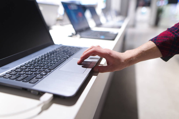L'homme contrôle l'ordinateur avec un pavé tactile. La main d'un homme utilise un ordinateur portable dans le magasin d'électronique. L'acheteur choisit un ordinateur portable dans un magasin de technologie
 - Photo, image