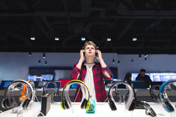 entscheidet sich ein junger Mann für ein Headset in einem modernen Geschäft. Kopfhörertest. - Foto, Bild