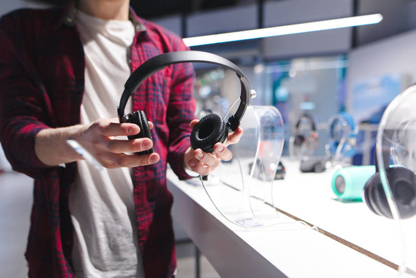 Muž drží černá sluchátka na pozadí v obchodě. Nákup sluchátek v úložišti tech. - Fotografie, Obrázek