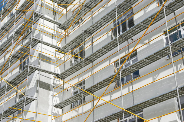 Σκαλωσιές κοντά σε ένα νέο σπίτι, το κτήριο εξωτερικά, βιομηχανία κατασκευής και επισκευής, λευκό τοίχο και παράθυρο, κίτρινο σωλήνα - Φωτογραφία, εικόνα