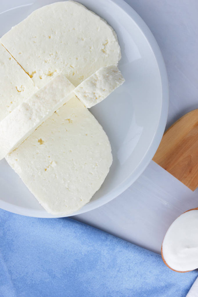 Τυρί, μέλι και ξινή κρέμα, φέτα σε λευκή πινακίδα, μαλακό τυρί σε λευκό φόντο, ξύλινο κουτάλι με ξινή κρέμα, γαλλικό πρωινό, μπλε πετσέτα, μέλι στα υαλικά, κενό για σχεδιαστής - Φωτογραφία, εικόνα