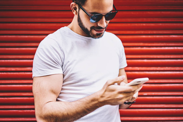 Handsome man in white shirt with copy space for young brand name reading income message checking mail on smartphone,hipster guy networking and blogging via modern cellular spending time outdoors - Photo, Image