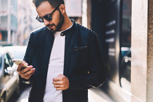 Handsome man checking mail on smartphone using application while spending time on city street,cropped image of male in trendy outfit sending text messages via cellphone chatting in networks outdoors - Fotó, kép