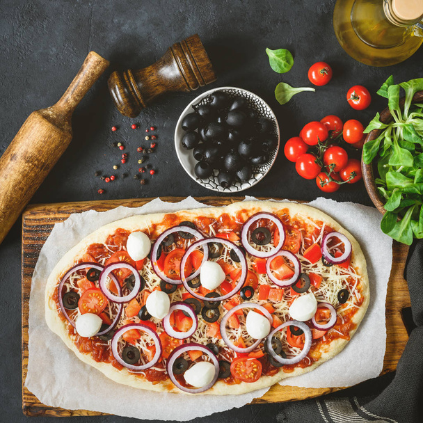 Pizza mit Tomaten, Mozzarella, schwarzen Oliven, Zwiebeln und Tomatensauce, von oben - Foto, Bild