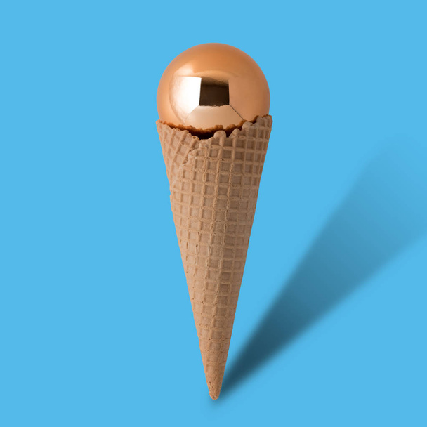 Ice cream cone with gold christmas ball on bright blue background - Foto, imagen