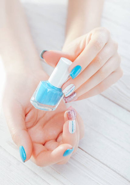 Mujer con manicura pastel sosteniendo esmalte de uñas azul. Tratamiento de la piel y concepto de cuidado corporal
. - Foto, imagen