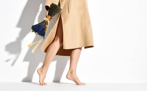 Beautiful female legs wearing brown yellow designers dress coat and bouquet of blue flowers lavender - Photo, image