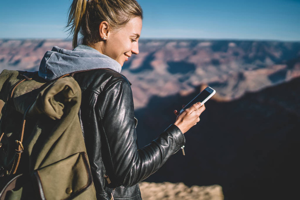 Smiling female tourist with backpack blogging in networks using good mobile connection in arizona national park,hipster girl checking mail on smartphone hiking in wild nature carrying rucksack - Photo, image