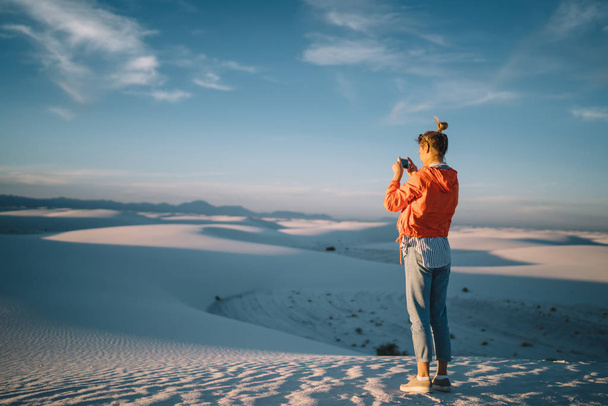 Back view of young female traveler making photo on scenic horizon over white dunes using smartphone camera,hipster girl taking photos during journey to White sands desert enjoying beautiful natur - Foto, afbeelding