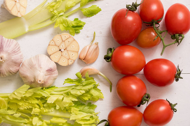 Fresh Vegetable Plate. cherry tomatoes on a white antique wooden background, a cutting board of celery parsley and garlic. Fresh greens for cooking. Healthy eating. Fresh spring summer lettuce - Photo, Image