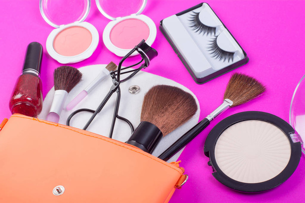 Bovenaanzicht van een make-up tas, met cosmetische schoonheidsproducten morsen uit op een roze achtergrond. - Foto, afbeelding