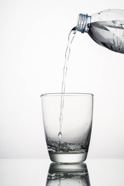 Close up de derramamento de água espirrando de vidro isolado sobre fundo branco
 - Foto, Imagem