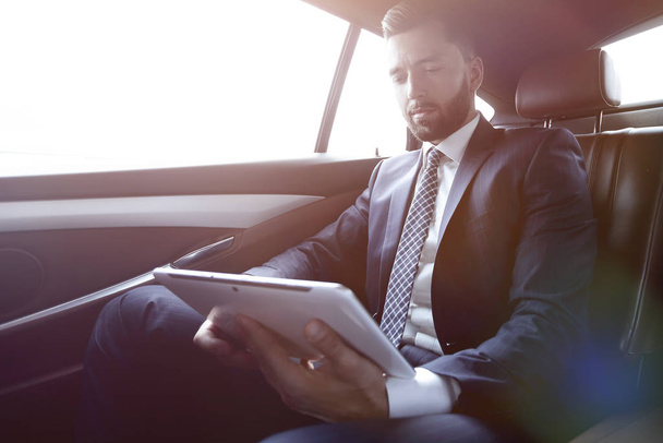 businessman working in the back seat of a car and using a tablet - Foto, afbeelding