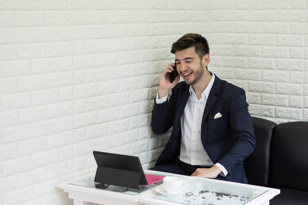 Jonge zakenman gebruiken smartphone terwijl u werkt op zijn laptop in kantoor - Foto, afbeelding
