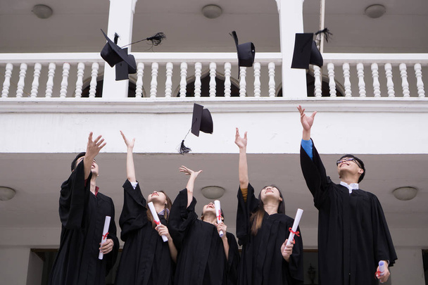 Группа успешных студентов с поздравлениями вместе бросают выпускные шляпы в воздух и празднуют. Концепция образования
. - Фото, изображение