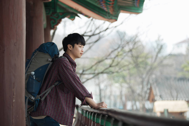 Ένας νεαρός άνδρας που κάνει ένα backpacking ταξίδι σε μια κορεατική παραδοσιακή κατοικία. - Φωτογραφία, εικόνα