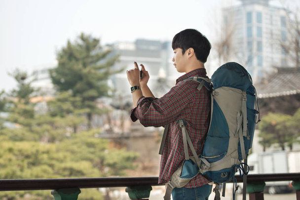 Un joven haciendo un viaje de mochilero en una casa tradicional coreana. Estoy tomando fotos usando mi teléfono inteligente
. - Foto, Imagen