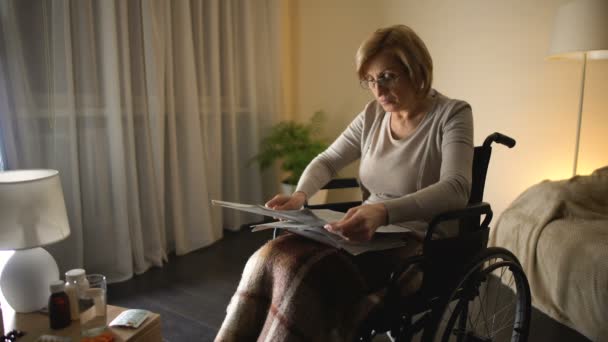 Old woman sitting in wheel chair and reading newspapers at home, health problem - Video
